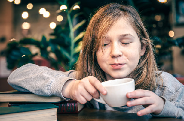 一个小女孩坐在咖啡馆里喝茶。图片下载