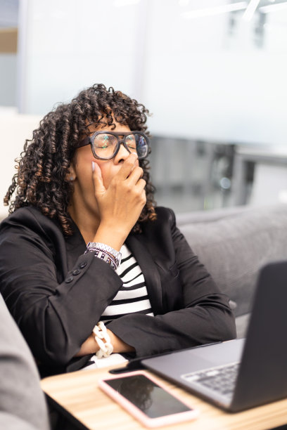 加勒比卷发年轻女子在沙发上用笔记本电脑工作图片下载