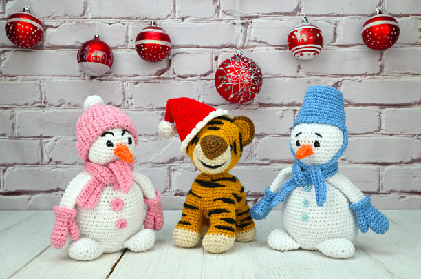 一只戴着新年帽的编织的老虎坐在两个雪人之间。在他们身后，挂着一个圣诞球花环图片下载