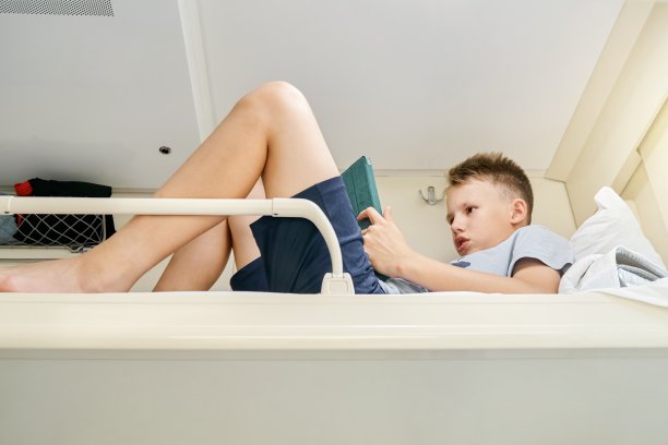 男孩躺在火车顶部的架子上通过平板电脑阅读电子书图片下载