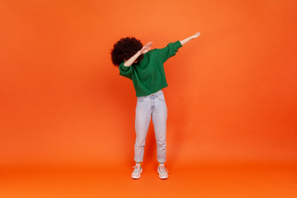 一名留着非洲式发型、穿着绿色毛衣的女子的全身肖像，展示了热门的网络表情包姿势，庆祝成功胜利，轻拍潮流。图片下载