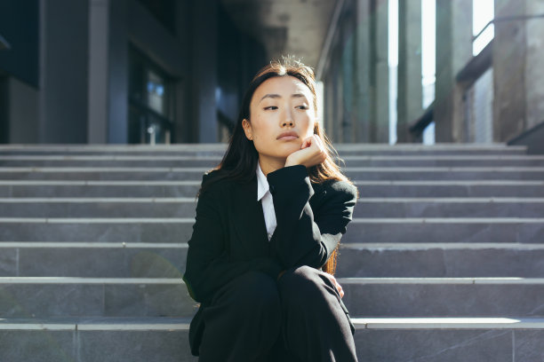 年轻美丽的亚洲妇女沮丧和悲伤坐在楼梯的办公中心，沮丧的商业妇女解雇图片下载