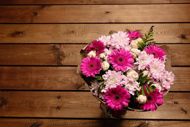 一大束美丽的菊花，非洲菊，玫瑰和蕨类植物，粉红色和紫色的颜色包裹在棕色的牛皮纸在木制的背景上。假期明信片。特写镜头图片下载