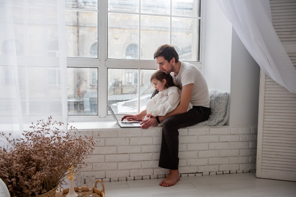 父亲和女儿坐在靠近窗户的白色木质窗台上玩笔记本电脑图片下载