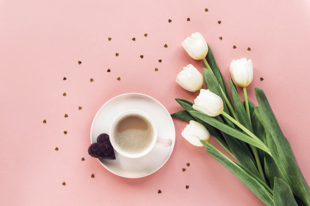 咖啡杯，心形巧克力饼干，白色郁金香花和粉色背景上的金色纸屑。情人节的概念。俯视图，平躺图片下载