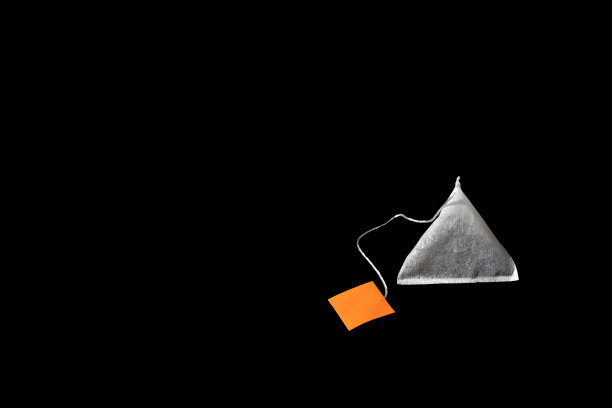 金字塔茶袋与橙色标签孤立在黑色背景。图片下载