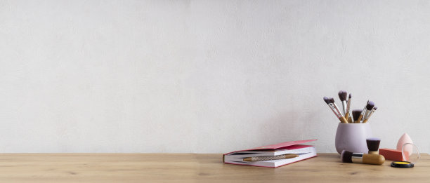 化妆用具，刷子，口红，紫色的文件夹，粉色的笔记本放在木制的桌子上，白色的空墙上。免费的背景图片下载