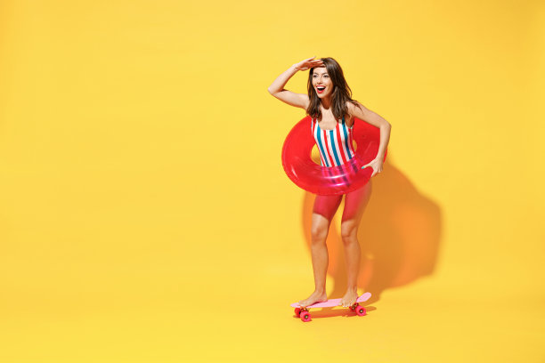 全长快乐年轻性感的女人苗条的身体穿红蓝色泳衣摆姿势与充气环溜冰孤立在生动的黄色墙壁背景工作室。夏季酒店泳池、海景、日光浴的概念。图片下载