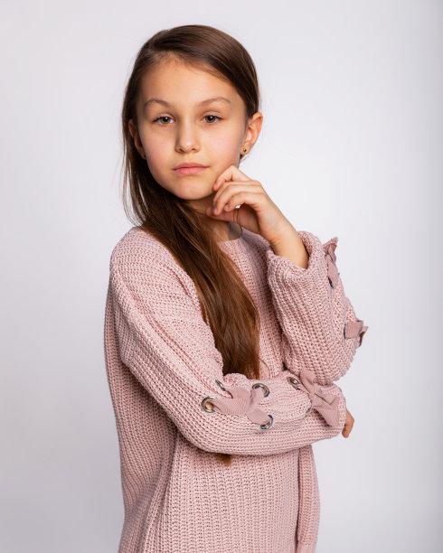 一个快乐微笑的小女孩的肖像。可爱的8岁小女孩的表情穿着粉红色的毛衣孤立在灰色的背景上图片下载