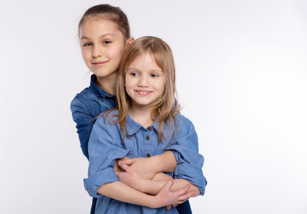 两个快乐的朋友或姐妹，小女孩拥抱着。一起有乐趣和摆情感的白色背景，快乐的微笑，友谊和关系的生活方式的人的概念图片下载