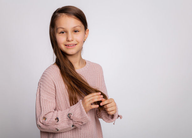 一个快乐微笑的小女孩的肖像。可爱的8岁小女孩的表情穿着粉红色的毛衣孤立在灰色的背景上图片下载