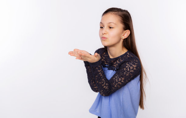 白种人小女孩看着镜头用手在空中飞吻很可爱。白色背景上的爱的表达图片下载