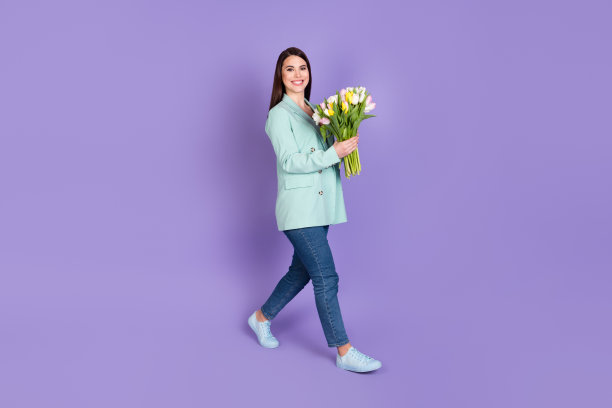 全尺寸的侧面照片，深褐色的女人走空的空间持有郁金香穿牛仔裤孤立在紫色的颜色背景图片下载