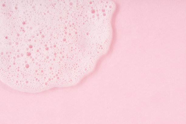 白色清洁剂泡沫滴在粉红色的背景上。图片下载