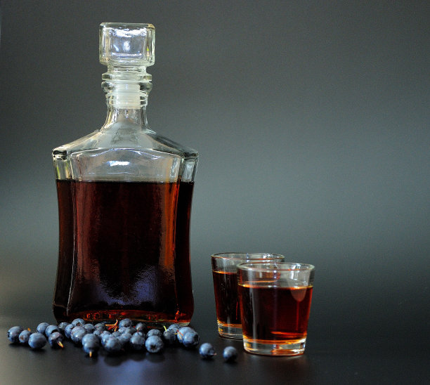 蓝莓利口酒，自制的烈性酒，装在两个玻璃杯和一个黑色的玻璃瓶里，旁边放着一串成熟的野生浆果。图片下载