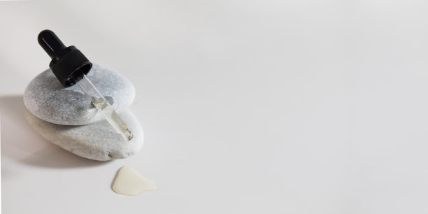 一滴皮肤用的血清从放在石头上的吸管流下来。副本的空间。图片下载