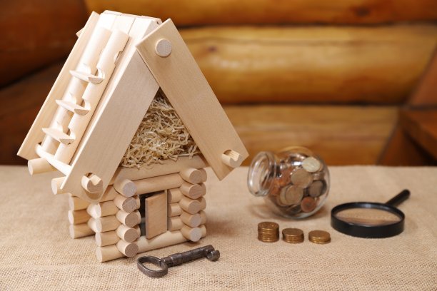 一个木头房子模型旁边的玻璃罐硬币。图片下载