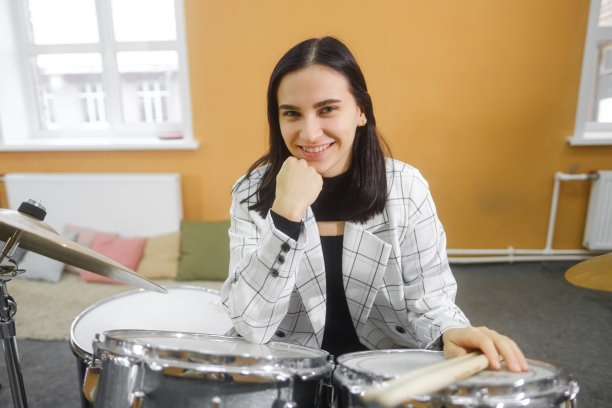 一幅年轻美丽的成年女子的肖像，站在一套鼓后面。爱好和消遣。图片下载