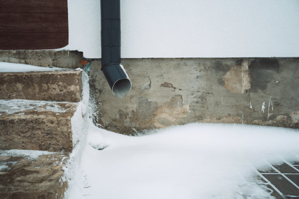白色房屋上的灰色落水管，背景是混凝土门廊和雪图片下载