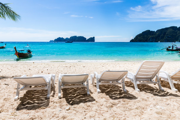 白色沙滩椅在SAN上，蓝色的天空和山的背景图片下载