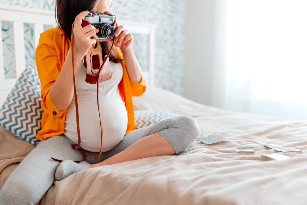 孕妇抱着复古相机躺在床上。怀孕的女孩在拍照。图片下载