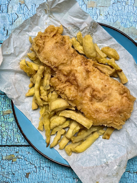 带盐和醋调料的外卖鱼和薯条的特写图片，用纸包裹在绿松石盘子上，不健康的外卖食品，油腻的鳕鱼和油炸薯条，绿松石木纹背景，高架视图图片下载