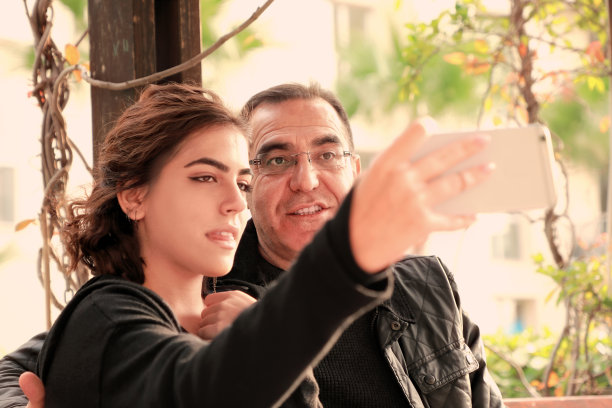 父亲和年轻的成年女儿在公园用手机自拍的户外照片图片下载