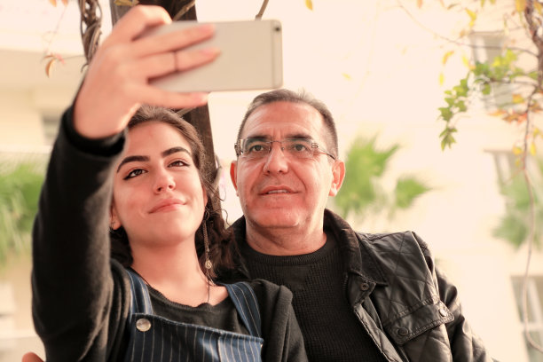 父亲和年轻的成年女儿在公园用手机自拍的户外照片图片下载