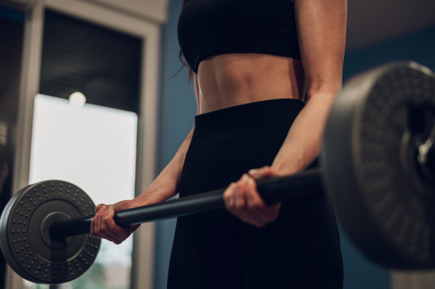 裁剪镜头的女性健身教练举起杠铃，而训练在健身房图片下载