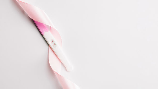 根验孕棒。孕妇试验阳性，白色背景上有粉色丝带。新的生活和新的家庭。母性、怀孕、节育概念。图片下载