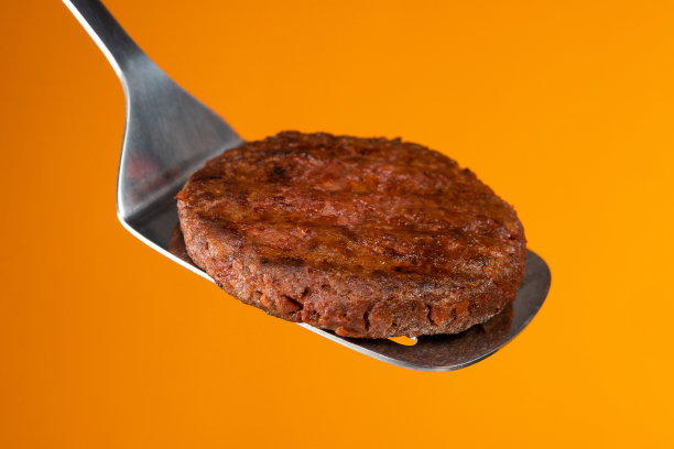 烧烤工具上的肉排-黄色墙壁上的抹刀柄。煮牛肉或猪肉小馅饼。生肉片做汉堡。特写照片。图片下载