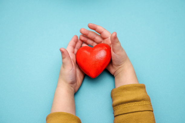 蓝色背景上孩子手中的一颗红心。爱、健康、捐赠的理念。图片下载