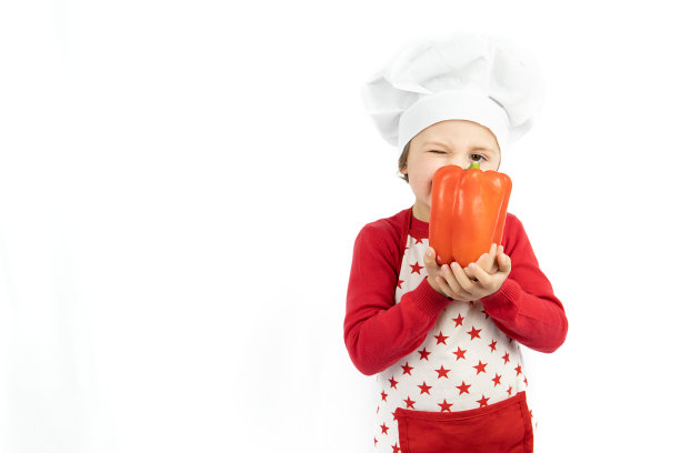 戴着厨师帽的快乐少年拿着红辣椒，孤立在白色的背景上。图片下载