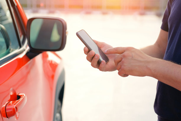 电话在一个男人的手中站在他的车外面。图片下载