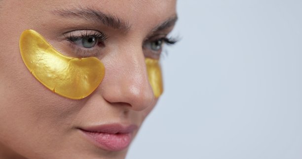 美丽微笑的女人在金色眼罩微笑的灰色背景的特写。美容护理和面部皮肤护理化妆品。图片下载