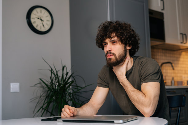 不健康的年轻自由职业者男性，喉咙痛，触摸脖子痛，感冒喉咙痛，感冒，感染，坐在桌子旁的笔记本电脑。图片下载