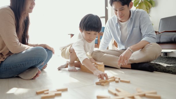 快乐的亚洲年轻父母，爸爸妈妈看着儿子玩玩具坐在家里的地板上。有爱心的父亲和母亲，有乐趣帮助可爱的小男孩建造木塔。给客厅享受游戏活动。图片下载