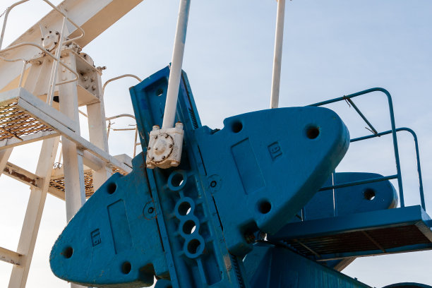 蓝天下的油泵的细节。颜色鲜艳的油泵产生石油或天然气。油泵在阳光明媚的日子工作。图片下载