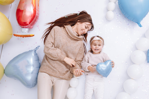 美丽的年轻妈妈和可爱的小女儿一起站在彩色的心形气球的背景上，拥抱和亲吻。生日，情人节，母亲节图片下载