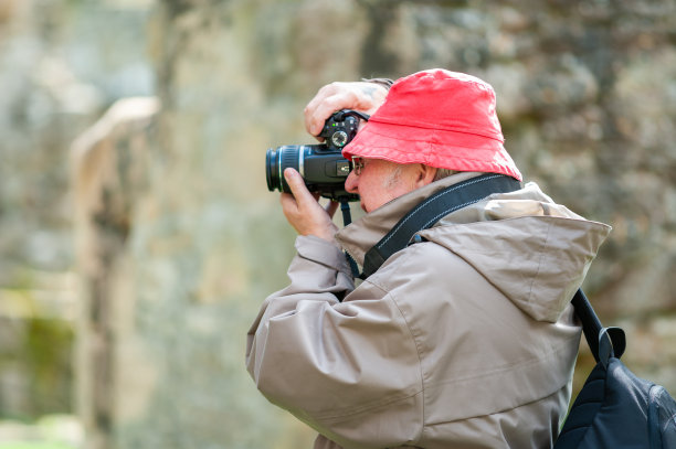 一位老人在古老的废墟中使用照相机。图片下载