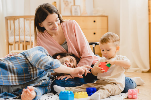 年轻的白人三口之家，父母，父母和蹒跚学步的婴儿，刚出生的儿子和女儿在家里玩开发游戏，花时间在一起。亲子关系的概念图片下载
