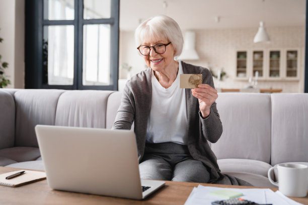 电子银行、电子商务。快乐的老老太太奶奶使用信用卡，在笔记本电脑上网上购物，买新衣服，礼物，支付国内账单，在家养老图片下载