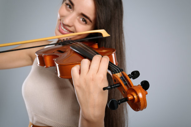 美丽的女人在灰色的背景上拉小提琴，特写镜头图片下载