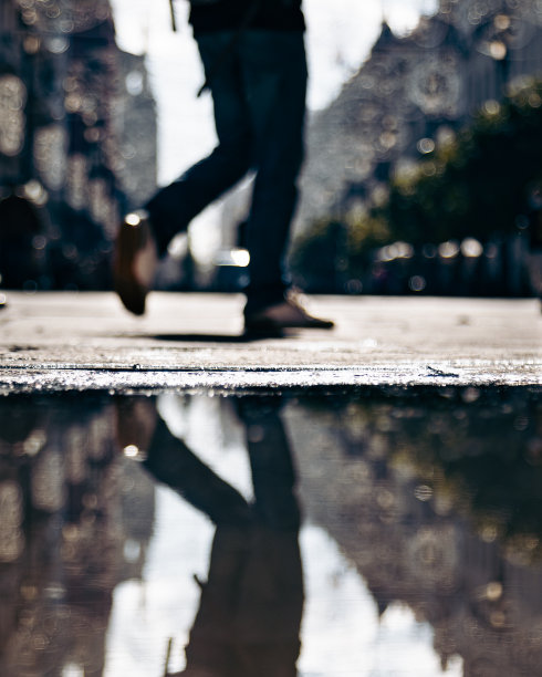 一个认不出来的男人的双腿模糊走在水坑旁边的街道上。图片下载