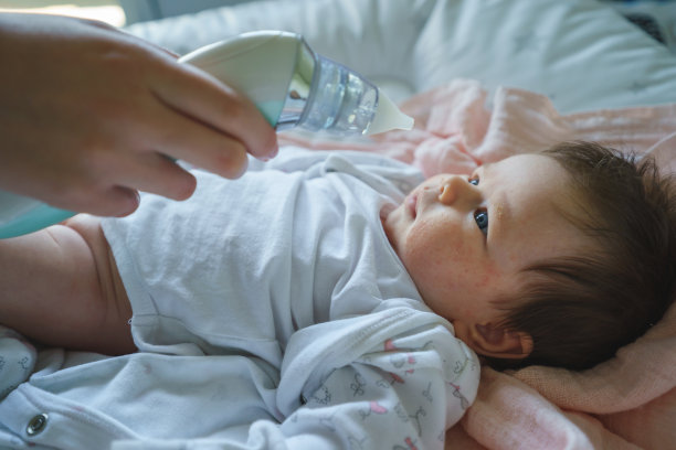 侧视不明女性母亲用电吸鼻器吸鼻涕，吸出婴儿的唾液清洁婴儿的鼻子，婴儿患有特应性湿疹，躺在床上图片下载