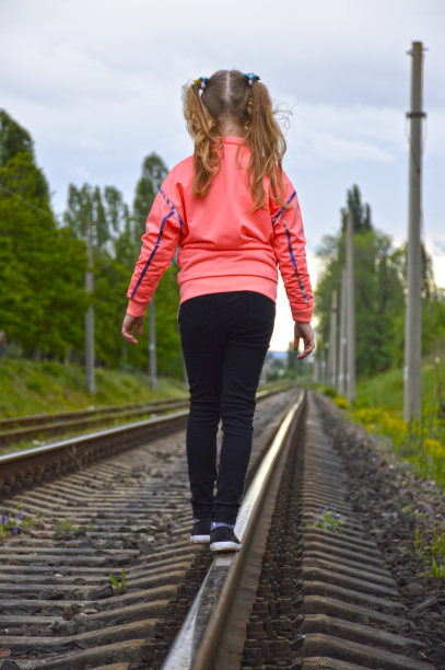 一个小女孩沿着铁轨行走，伸开双臂保持平衡图片下载