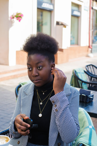 深色皮肤的迷人非裔美国女人，戴着黑色无线耳机，在一个户外咖啡馆图片下载