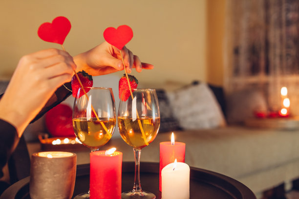 一名女子在家里为情人节庆祝装饰餐桌，把爱心和香槟酒放在玻璃杯里，点燃蜡烛图片下载