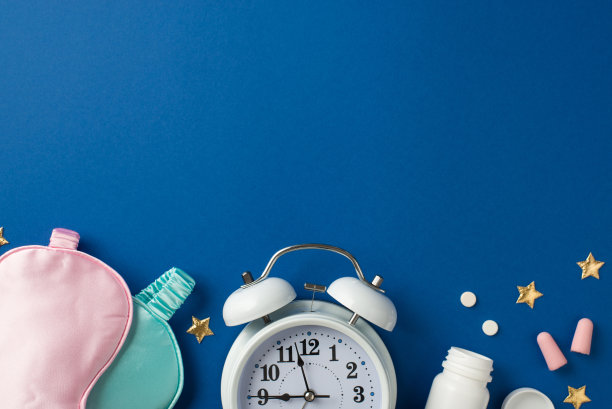 俯视图照片的形状，两个丝绸面具粉红色和浅蓝色，一个大的白色警报和两个粉色耳塞与管，两种药物和一个金色星星形状的五彩纸屑在深蓝色孤立的背景空白空间图片下载