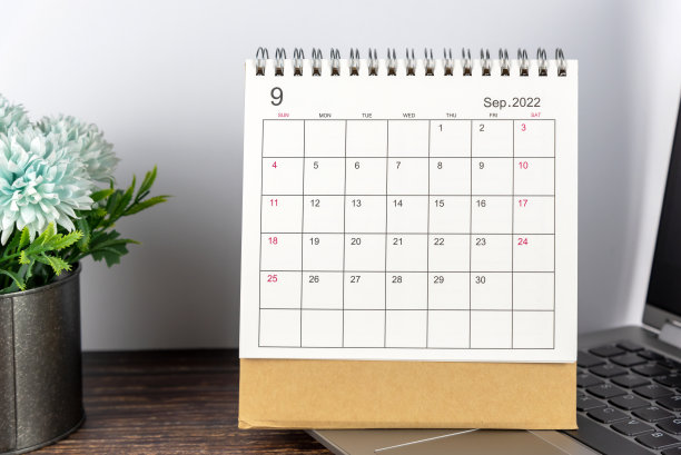 2022年9月日历日期与笔记本电脑和蓝色的花在黑色的花瓶在质朴的木桌上。图片下载